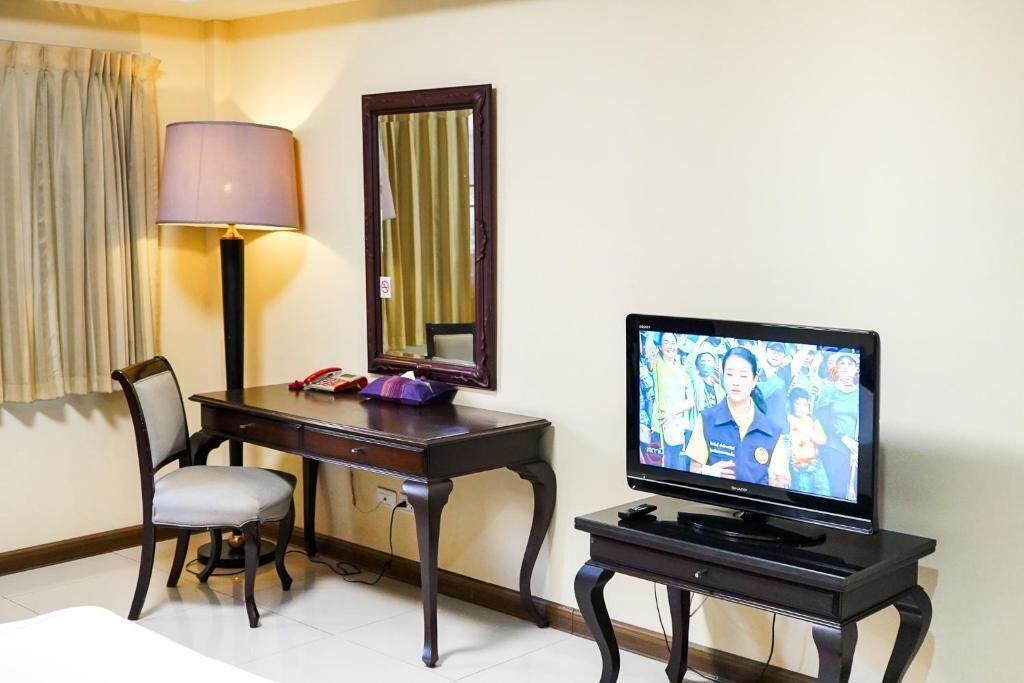 Habitación de hotel con televisión sobre un soporte, escritorio con lámpara, una silla y una cama.