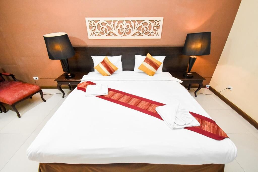 Habitación de hotel con una cama grande, dos mesitas de noche, dos lámparas, un adorno en la pared y una silla roja.