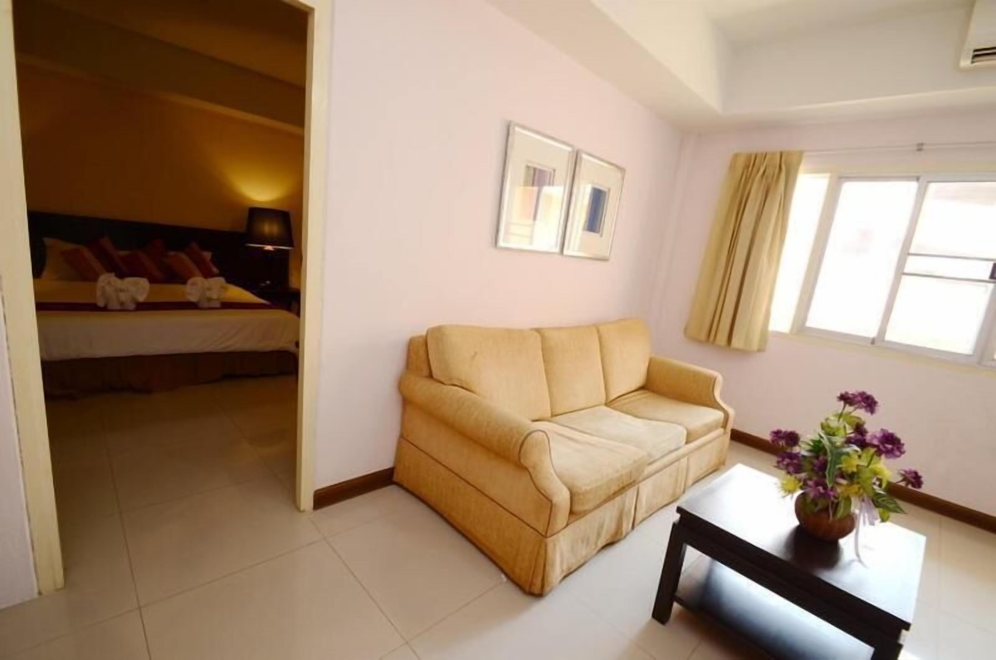 Una habitación con cama, sofá, una mesita y una ventana con cortinas.
