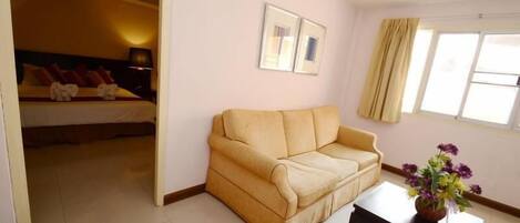 Una habitación con cama, sofá, una mesita y una ventana con cortinas.