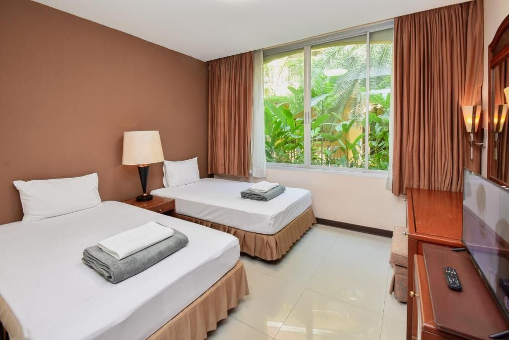 A hotel room with two beds, a TV, a lamp, and a window with curtains.