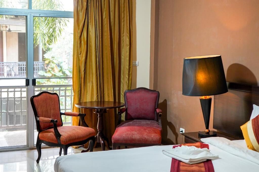 A hotel room with a bed, two armchairs, a small table, a lamp, and a view of the outdoors.