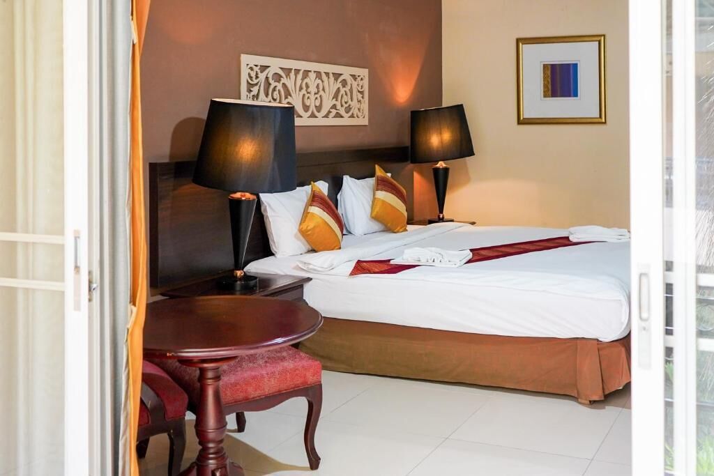 Una habitación de hotel con una cama, dos lámparas de noche, una mesa y una silla.