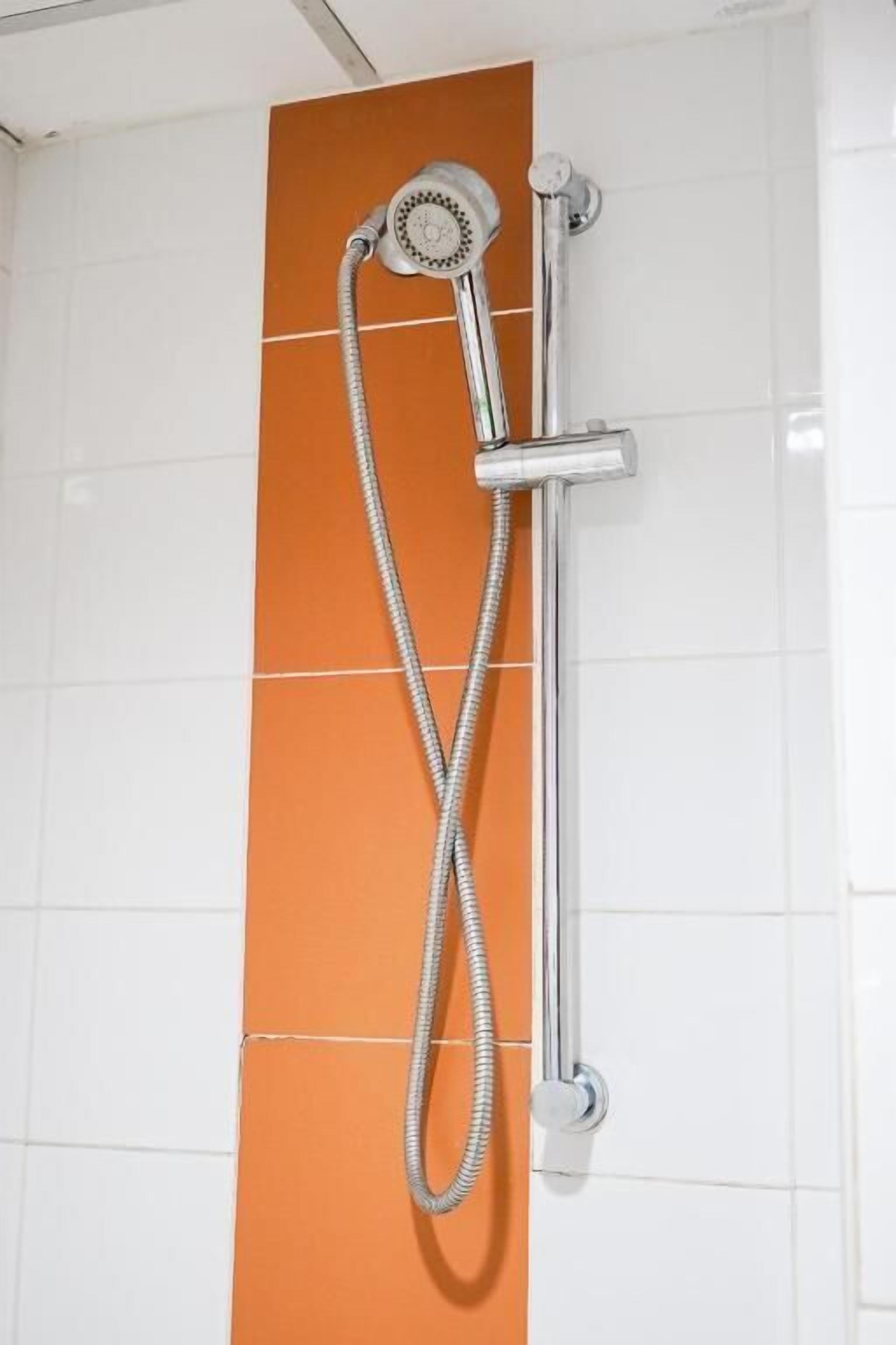 A shower with a chrome fixture and a flexible hose against a tiled wall with a vertical orange panel.