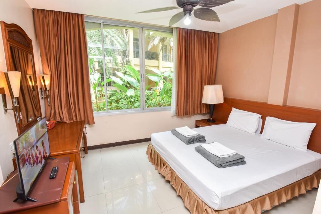 A hotel room with a bed, a television, a desk with a remote control, and curtains.