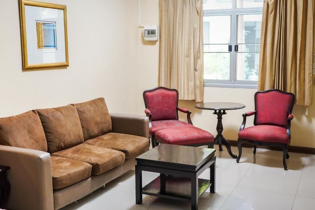 A living room with a brown sofa, two red armchairs, a small round table, and a window with curtains.