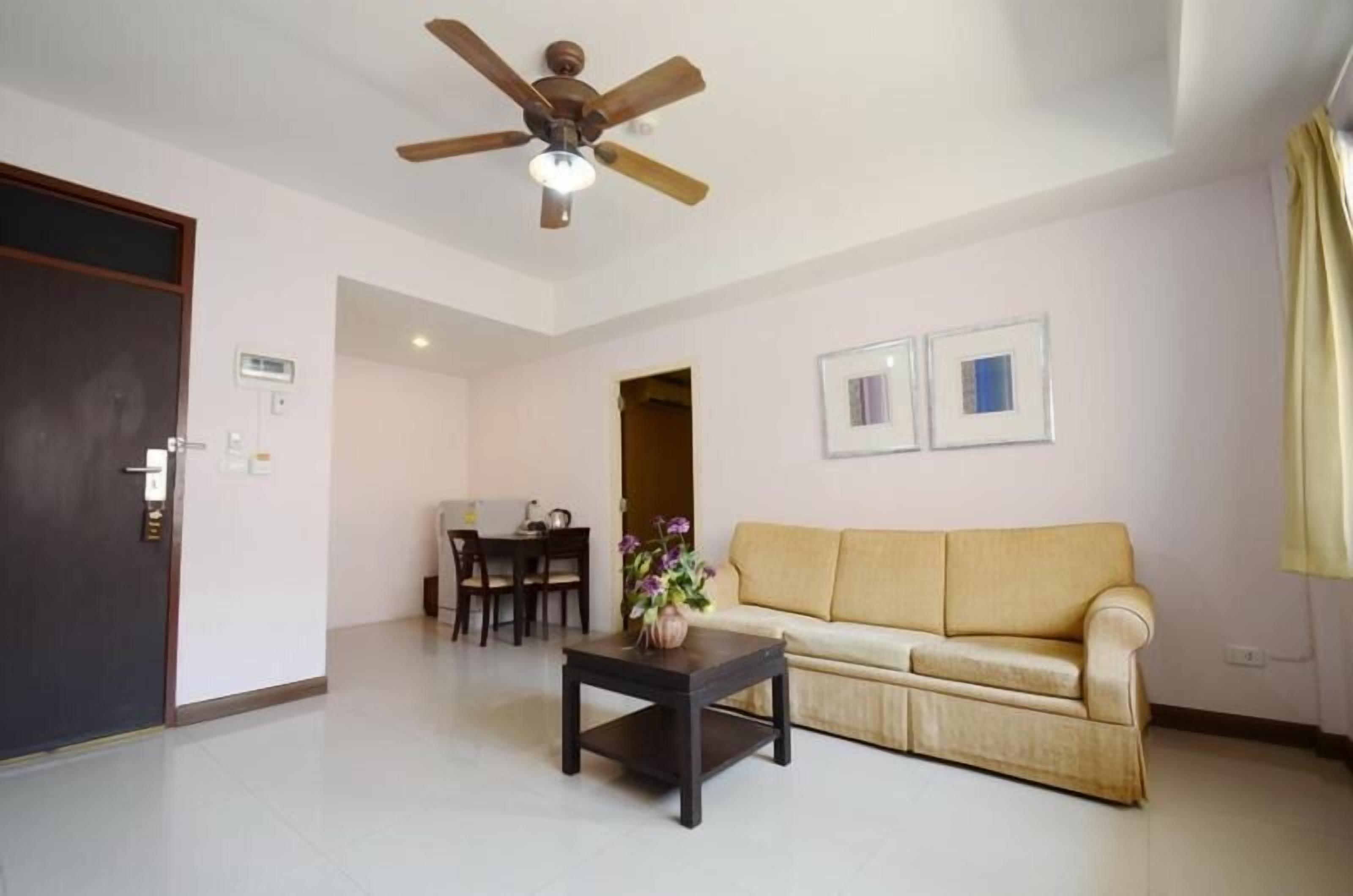 A living room with a sofa, a coffee table, a ceiling fan, and a dining area with chairs and a table.