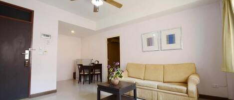 A living room with a sofa, a coffee table, a ceiling fan, and a dining area with chairs and a table.