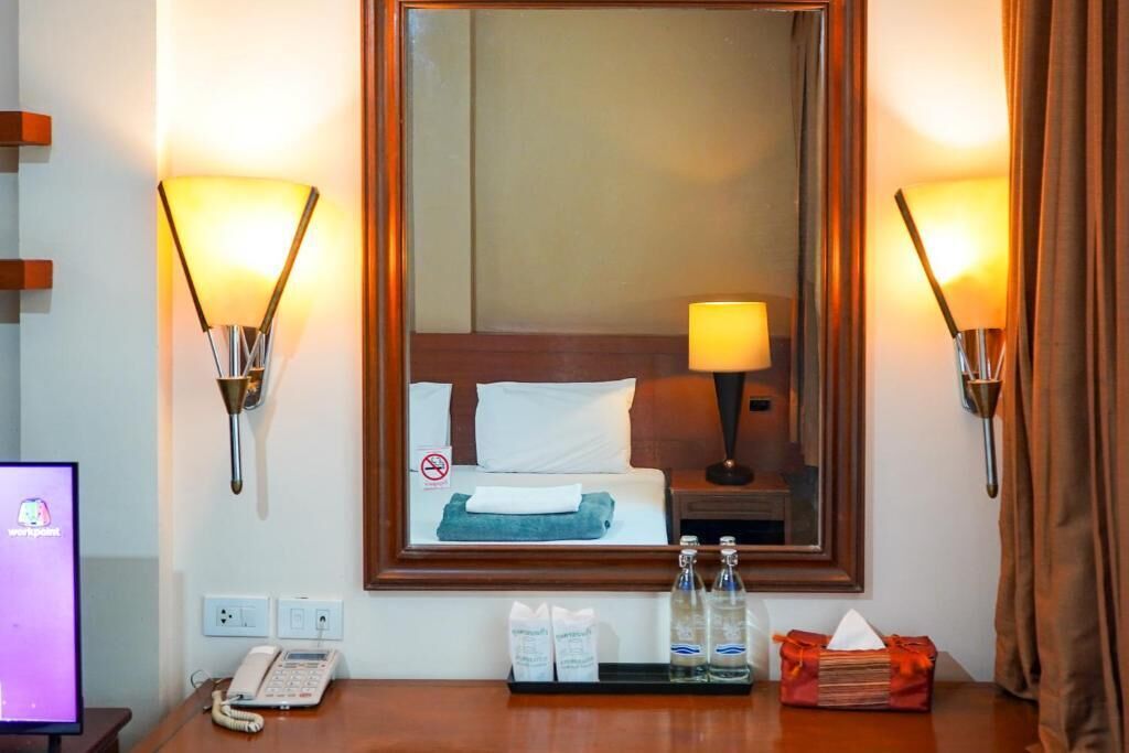Quarto de hotel com cama, luminária de cabeceira, espelho, telefone e bandeja com artigos de higiene pessoal.