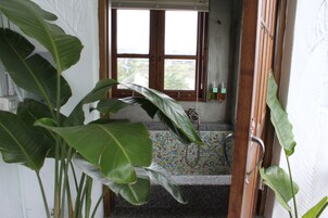 Un baño con piso de baldosas, zona de ducha y ventana con cortinas.