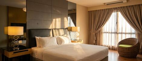 A hotel room with a large bed, two bedside lamps, a wicker chair, and a large window with curtains.