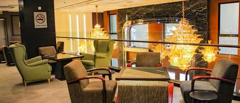 A hotel lobby with seating, a chandelier, a marble wall, and a view of a train.