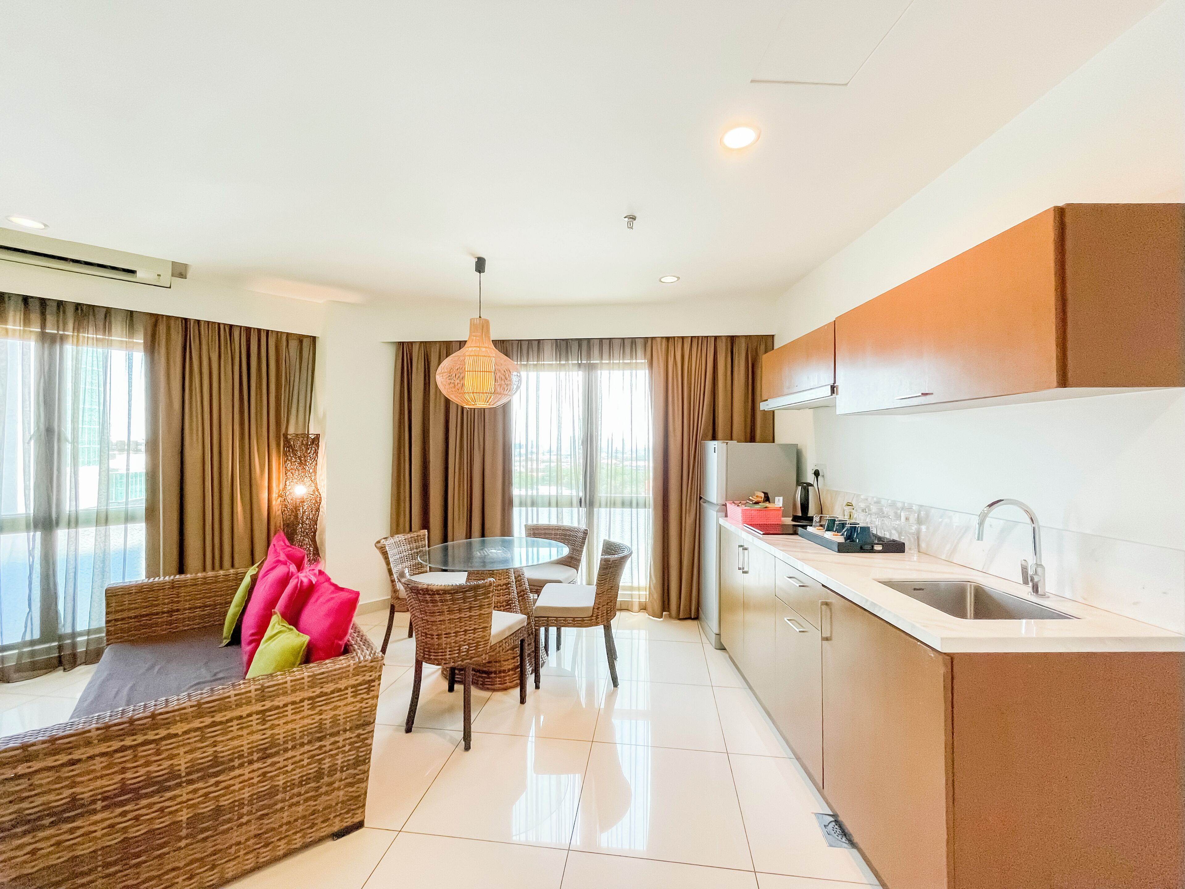 Una habitación de hotel moderna con zona de comedor, kitchenette y un ventanal con cortinas.