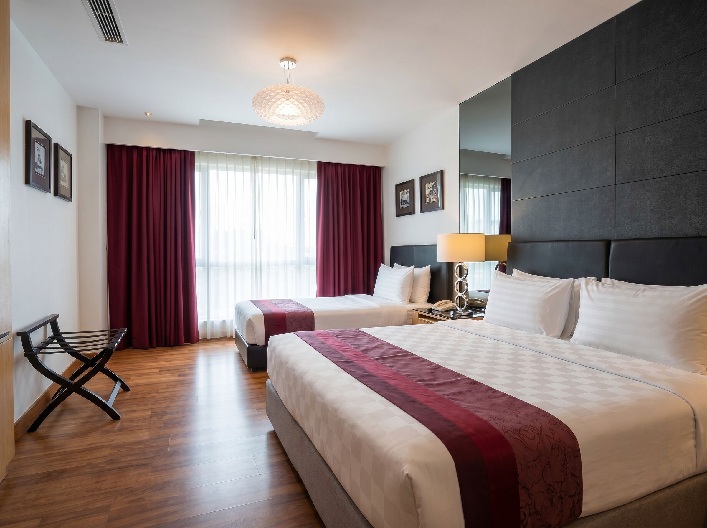 A hotel room with a large bed, a smaller bed, a desk with a lamp, a chair, and a large window with curtains.