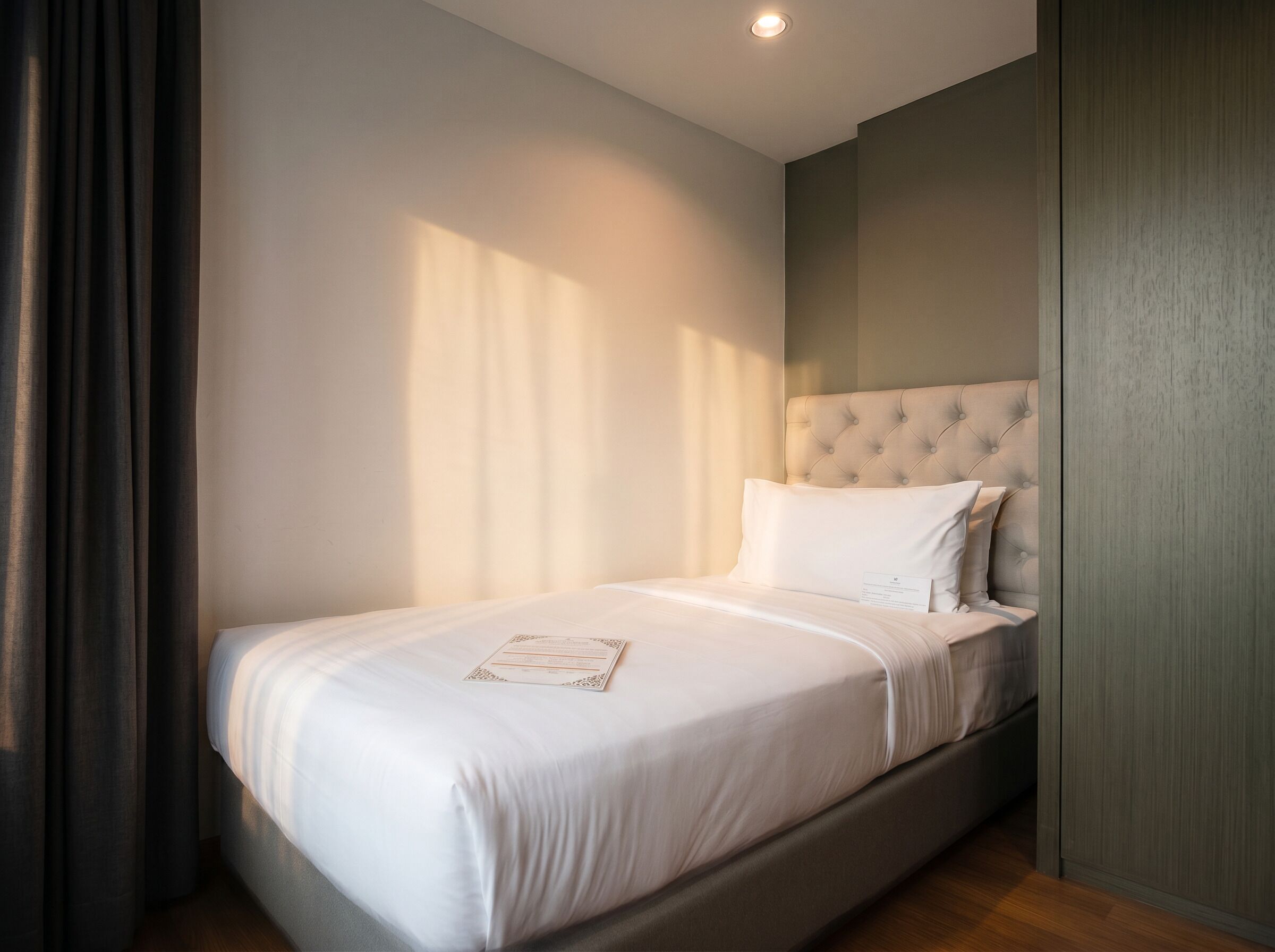 Un letto rifatto con cura in una stanza con testiera trapuntata, un comodino e un mobile a parete.