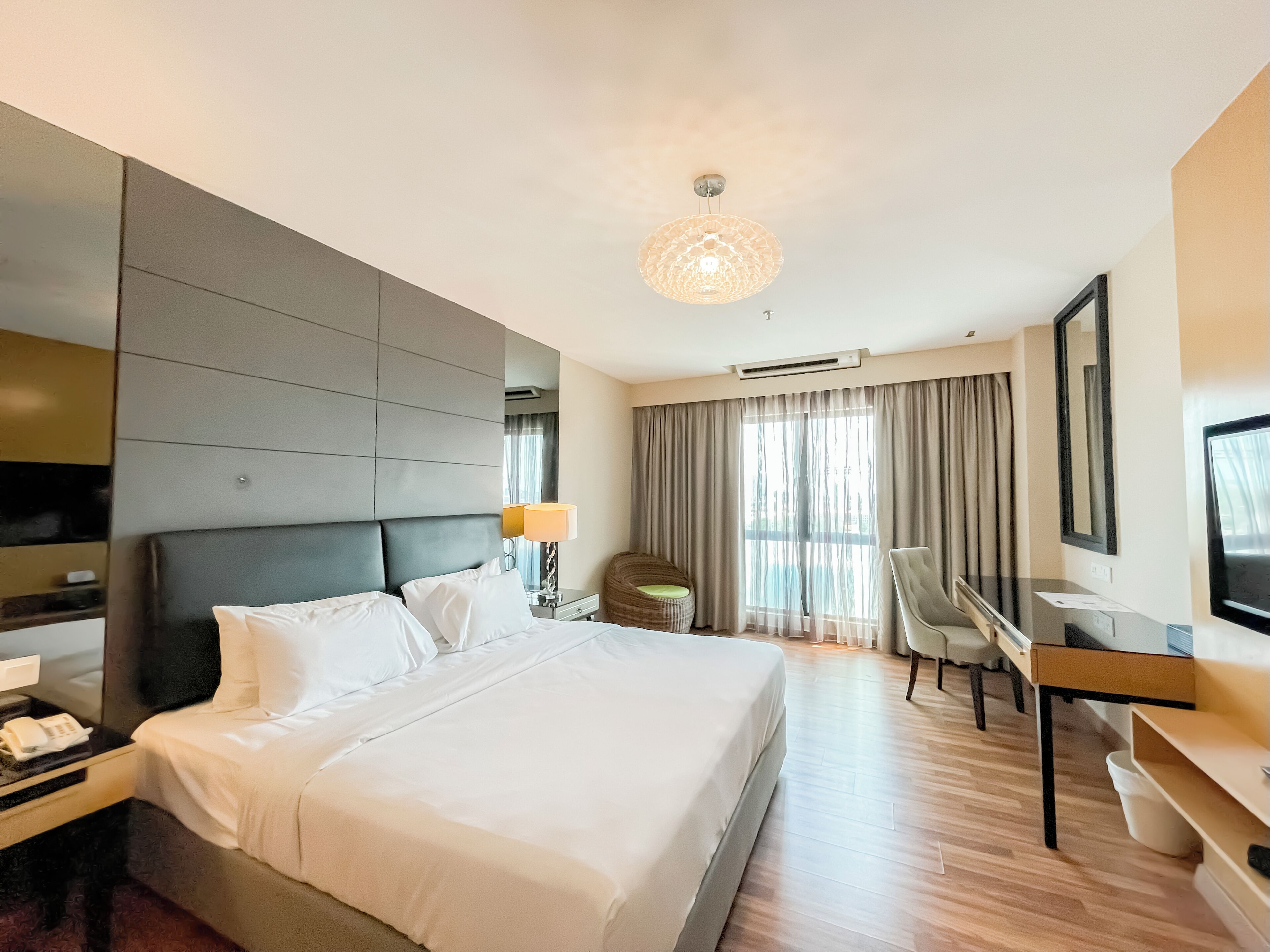A hotel room with a large bed, a desk, a chair, a television, and a window with curtains.