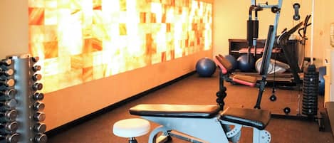 Un gimnasio con equipo de ejercicio, una banca y una pared con un diseño geométrico.