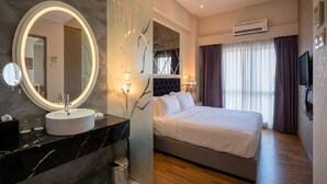 Una habitación de hotel moderna con un espejo redondo, un lavamanos de mármol, una cama con ropa blanca, un televisor y un equipo de aire acondicionado.