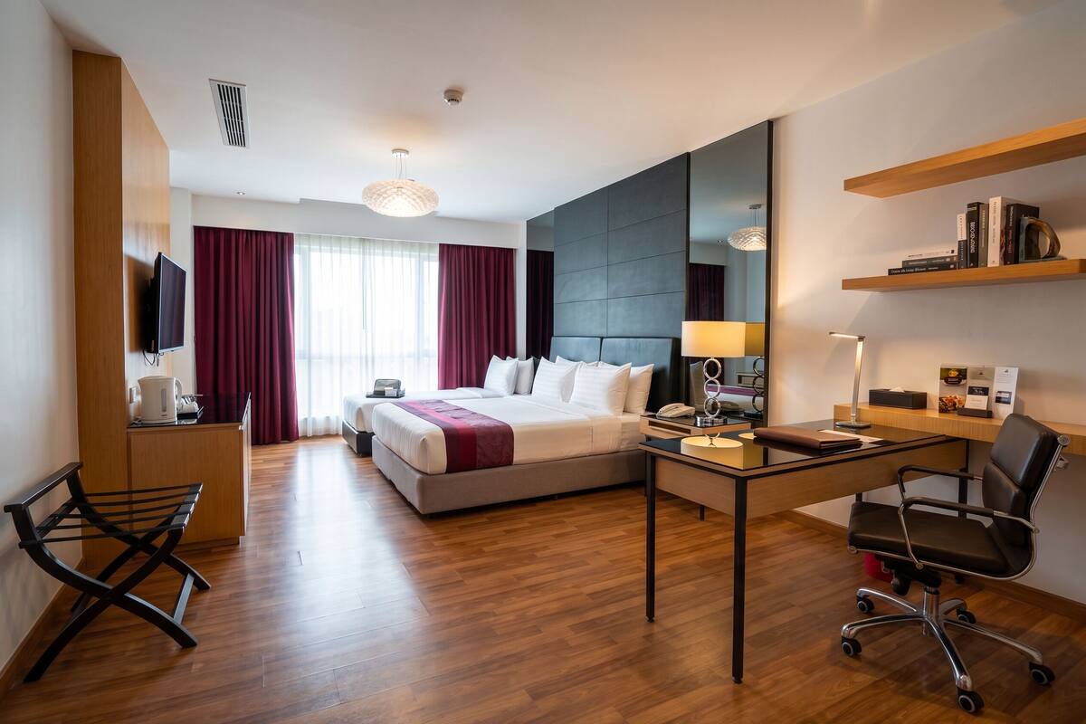 A hotel room with a bed, desk, chair, and a large mirror.