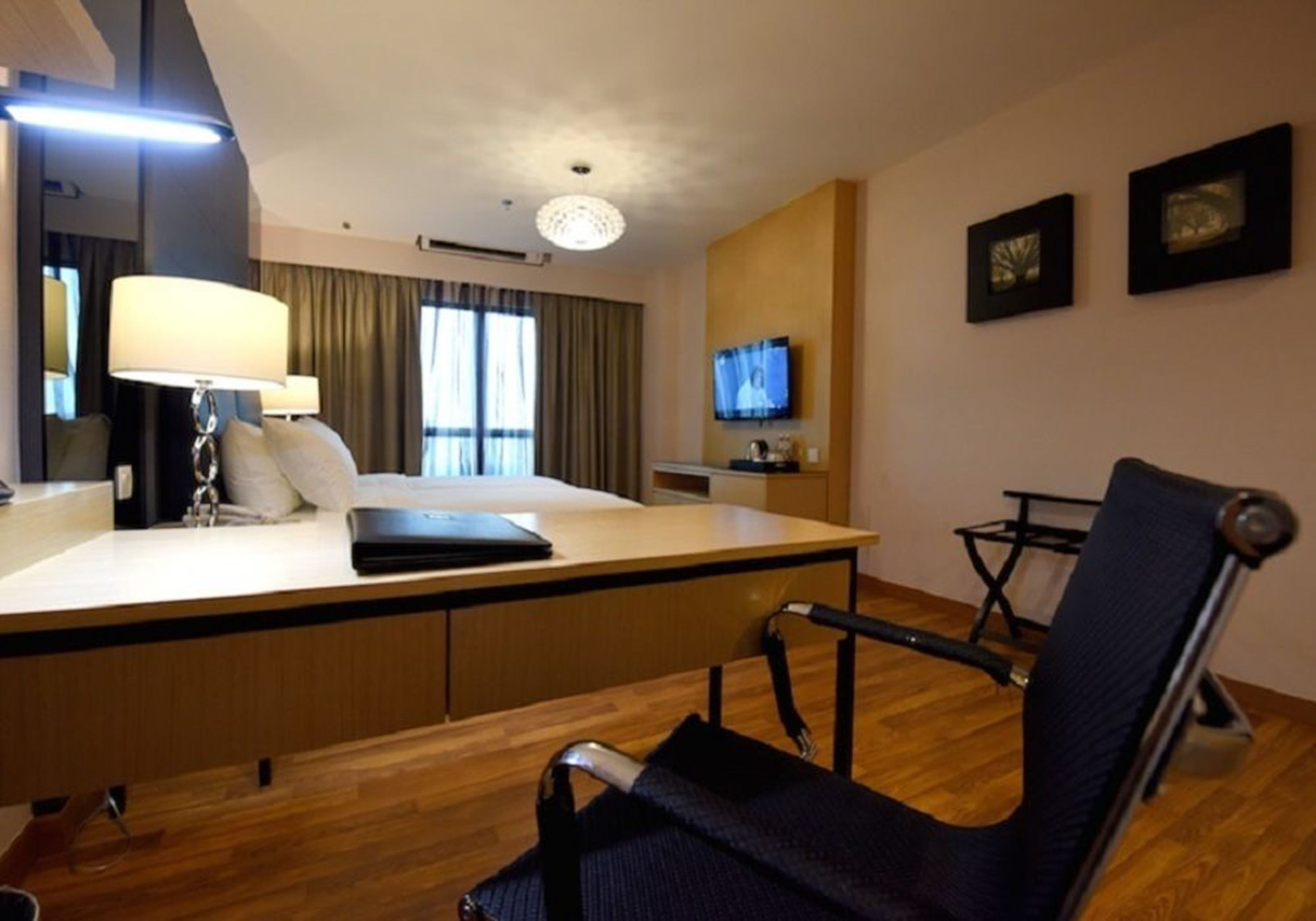 Een hotelkamer met een bed, een bureau met een laptop, een stoel, een televisie en kunst aan de muur.