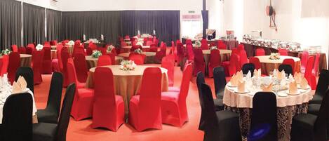 Un salón de banquetes con mesas redondas, sillas rojas y manteles blancos.