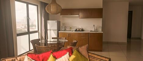 A modern living room with a sofa, a dining table, and a kitchen area with wooden cabinets and a refrigerator.