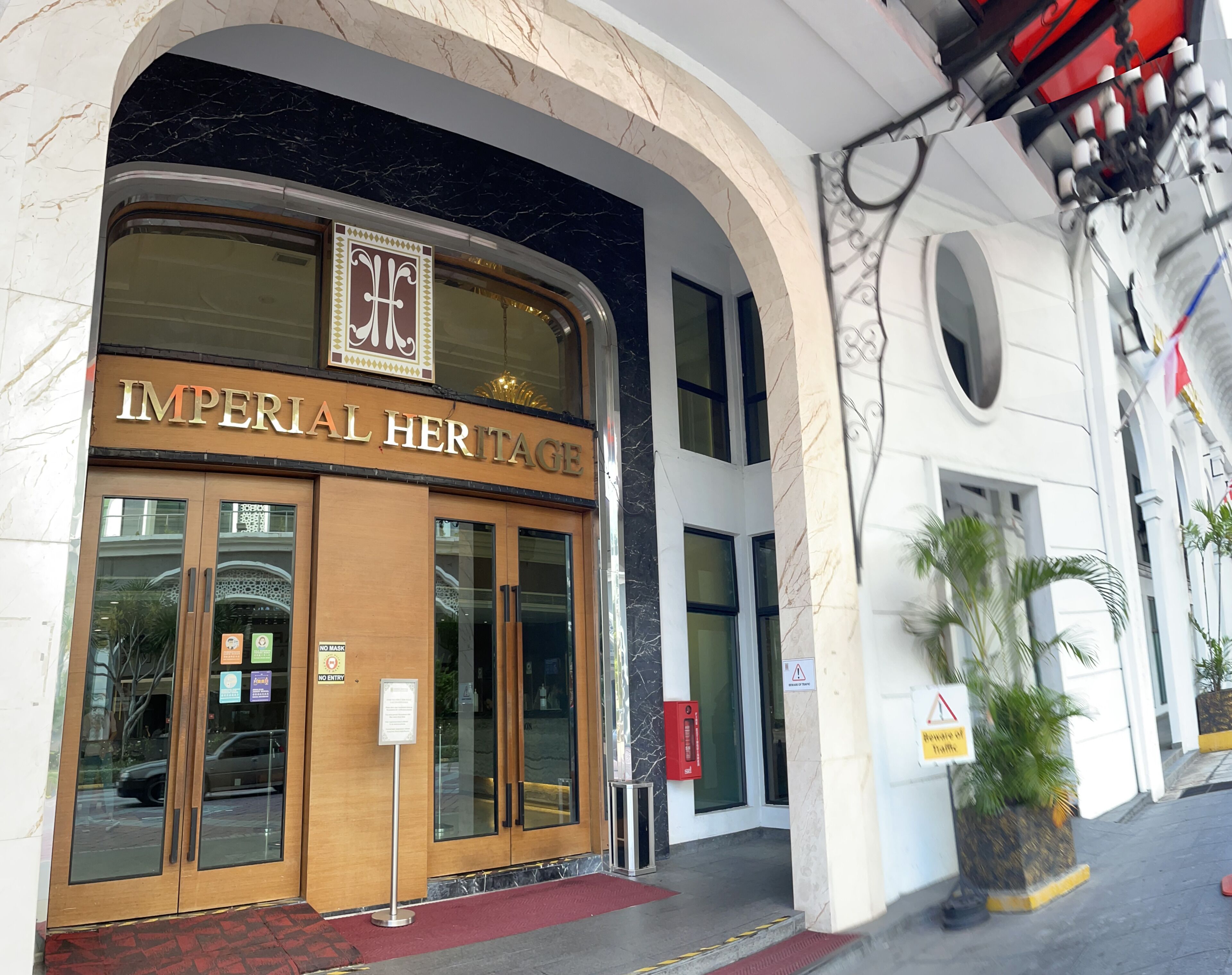 The exterior of the Imperial Heritage hotel with marble columns, a grand entrance, and a sign indicating no mask entry.