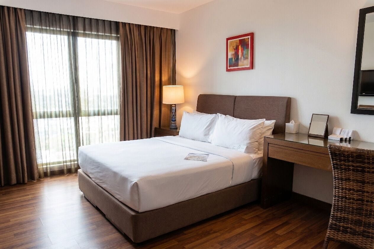 A hotel room with a bed, a desk, a chair, a lamp, and a painting on the wall.