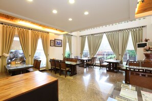 Un comedor de hotel con varias mesas y sillas, ventanas grandes con cortinas y techo de madera.
