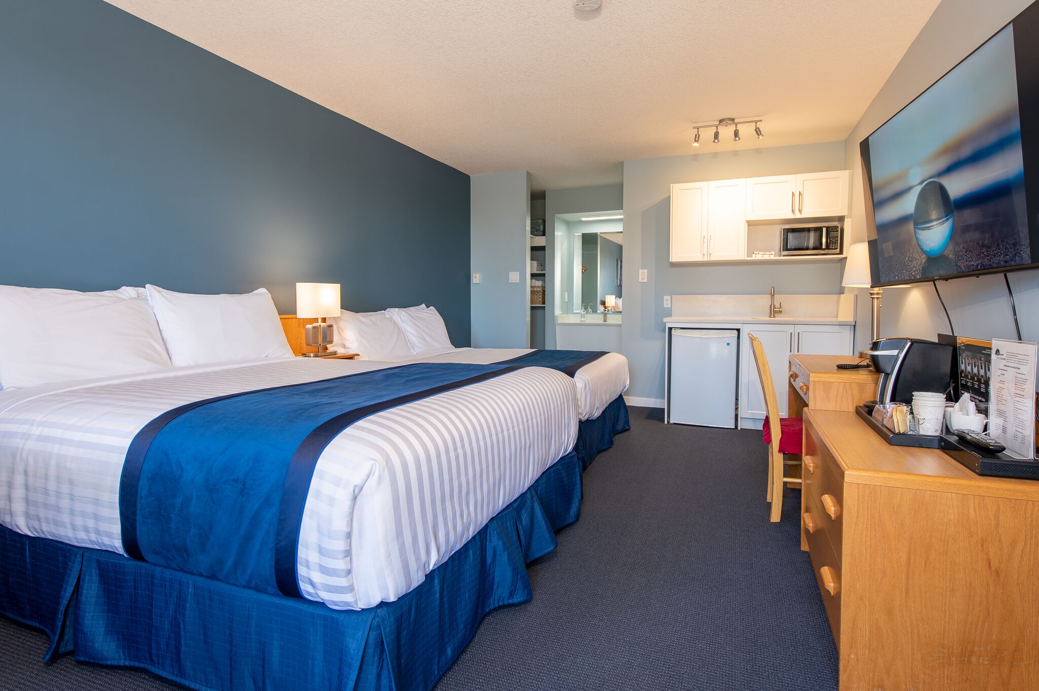 A hotel room with two beds, a desk, a microwave, and a TV.