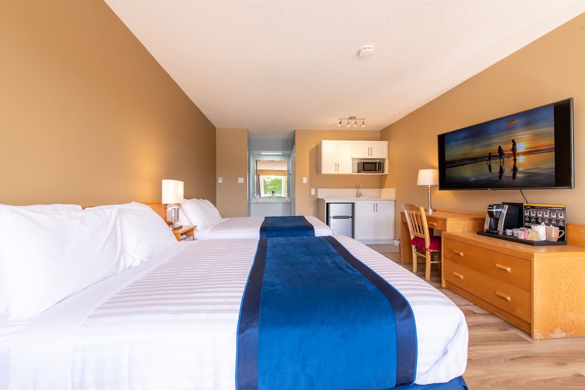 A hotel room with two beds, a desk, a chair, a television, and a kitchenette.
