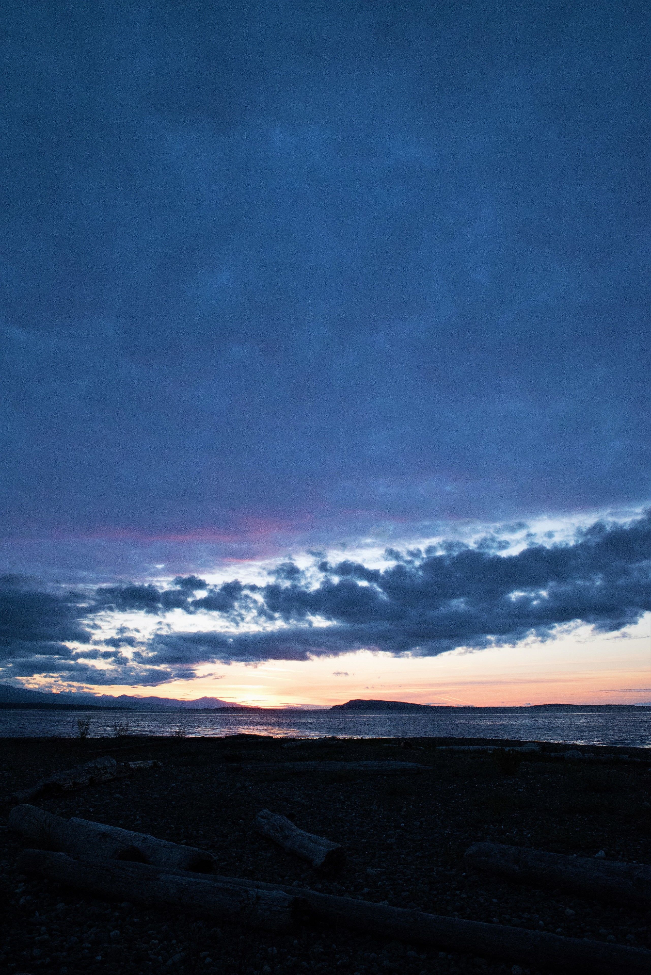 A beach with a rocky foreground and a sunset over the water.