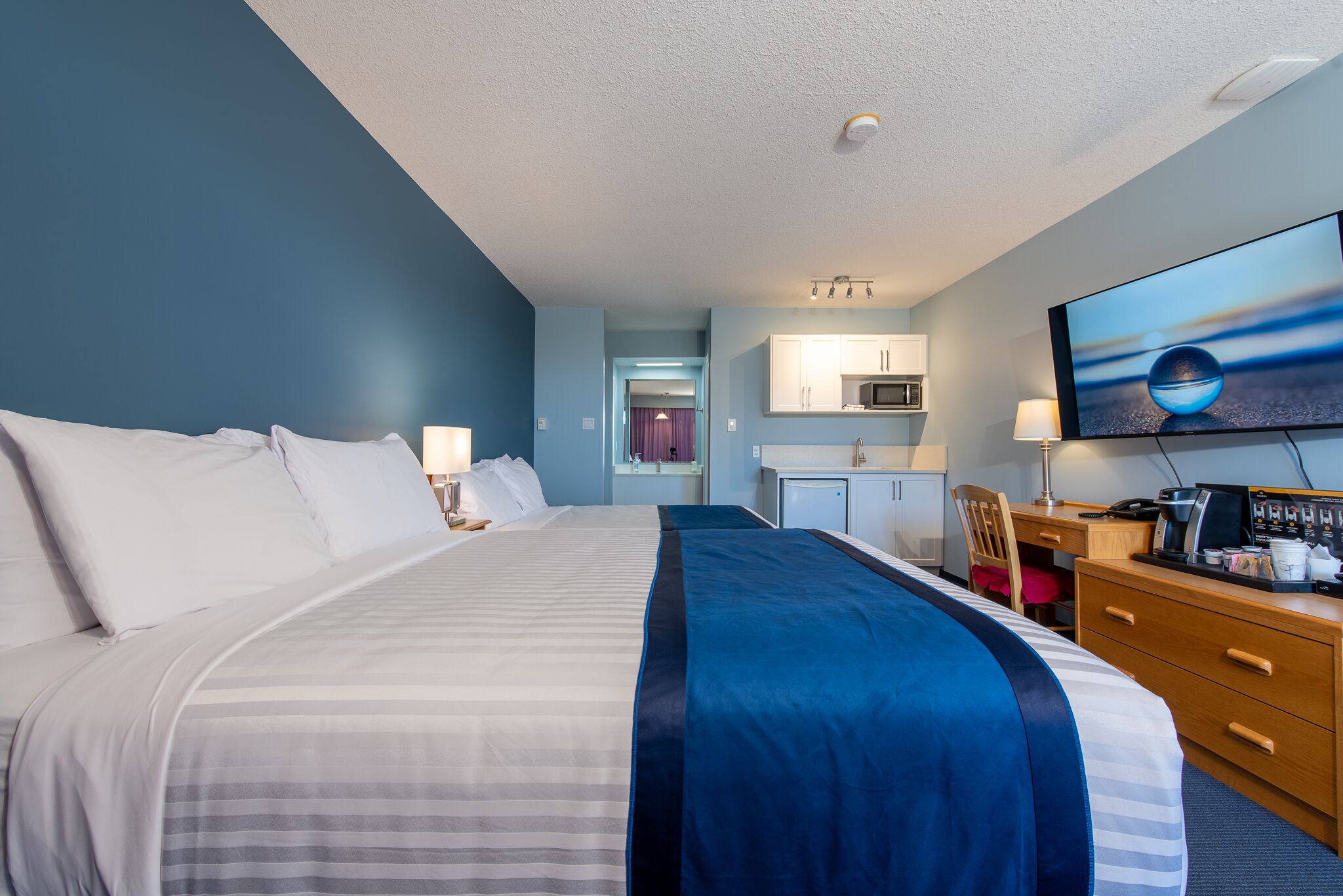 Ein Hotelzimmer mit einem großen Bett, einem Schreibtisch mit Computer, einem Fernseher und einer Küchenzeile.