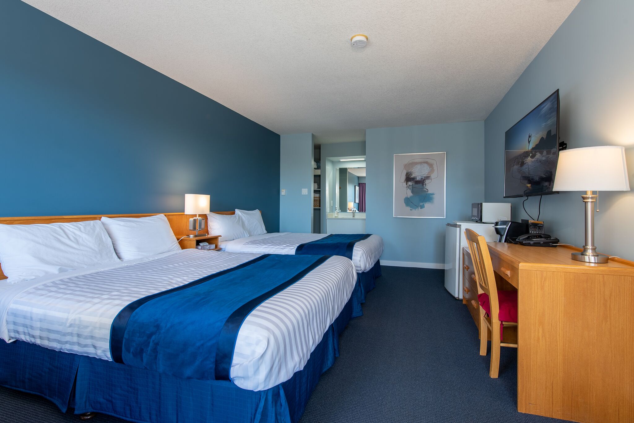A hotel room with two beds, a desk, and a chair.