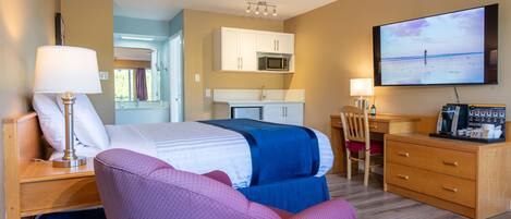 A hotel room with a bed, a desk, a chair, a TV, and a kitchenette.