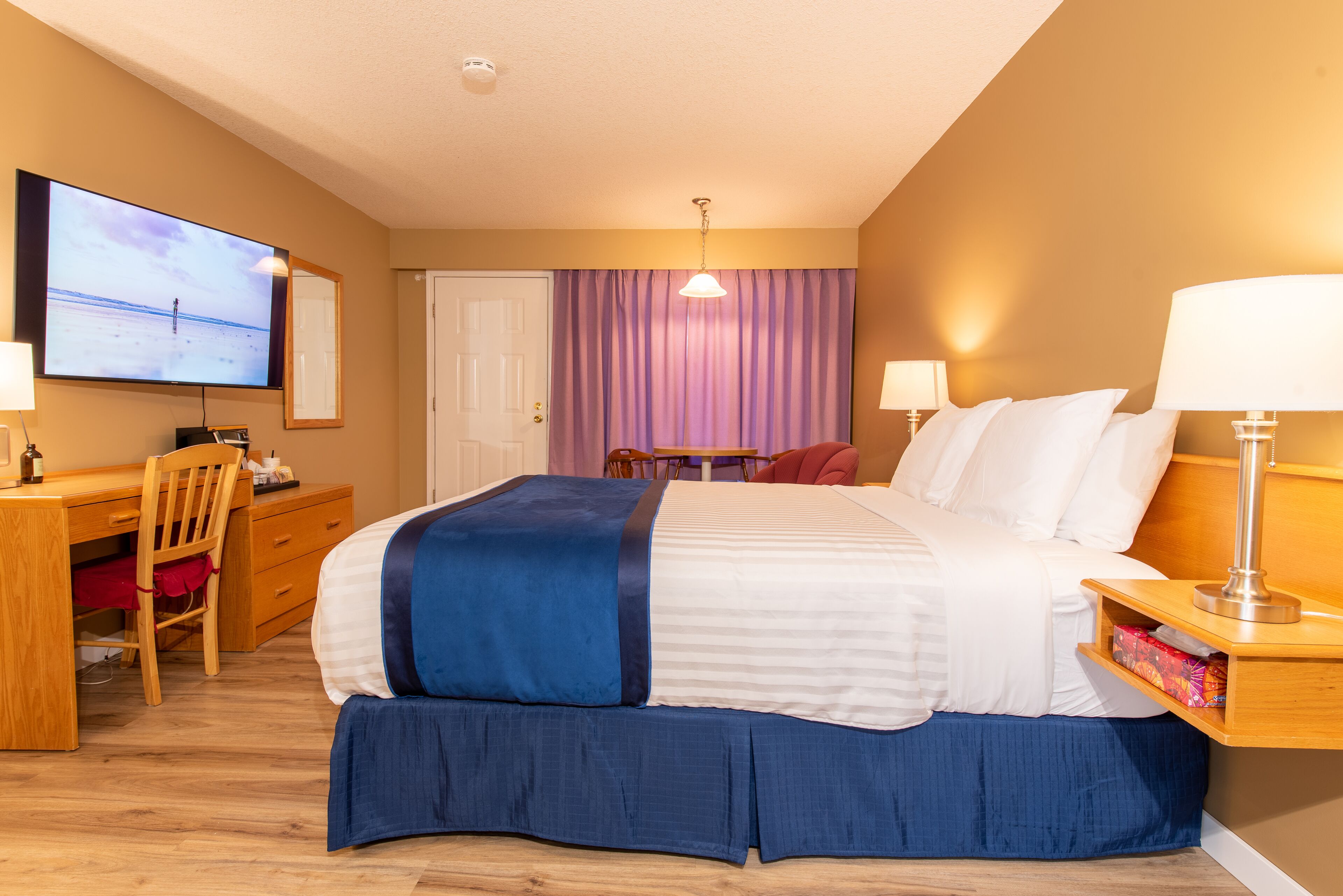 Una habitación de hotel con cama, escritorio, silla, televisor y cortinas.