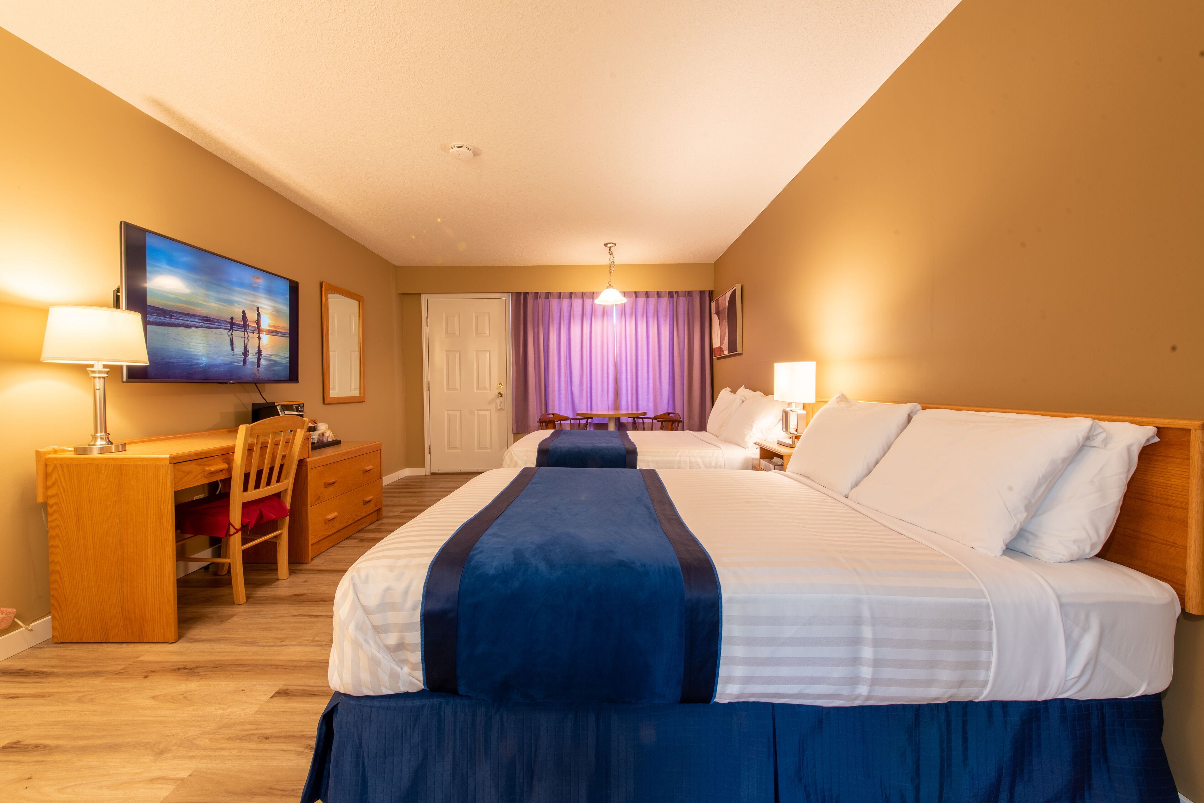 Habitación de hotel con dos camas, un escritorio, una silla, un televisor y una puerta.