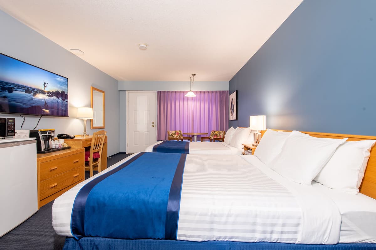 A hotel room with two beds, a desk with a computer, a chair, a TV, and a window with curtains.