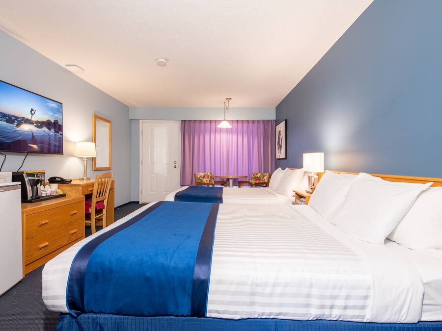 A hotel room with two beds, a desk with a computer, a chair, a TV, and a window with curtains.