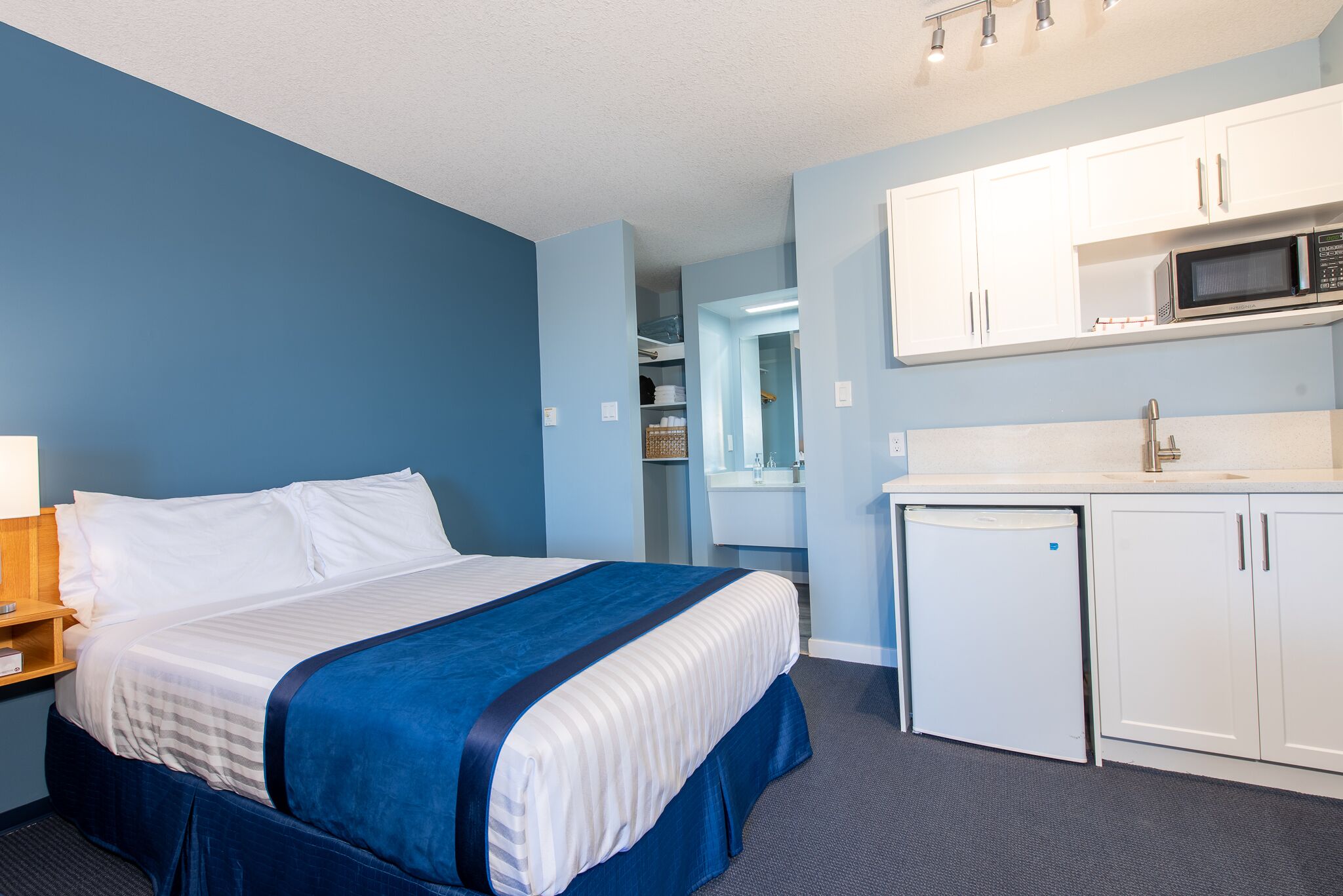 A hotel room with a bed, a desk, a microwave, a sink, and a storage cabinet.