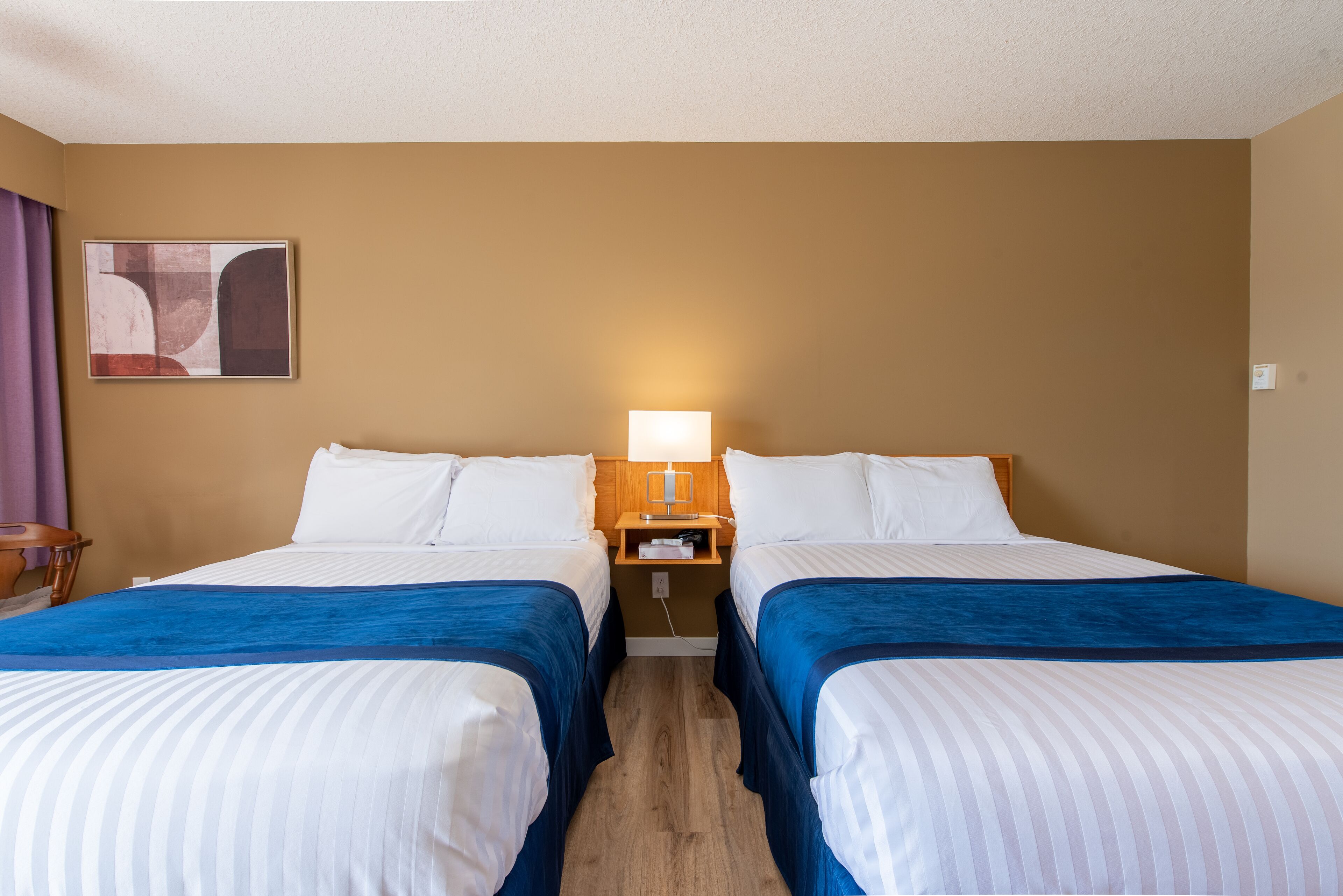 Ein Hotelzimmer mit zwei Betten, einem Nachttisch mit Lampe und einem Bild an der Wand.