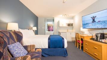 A hotel room with a bed, a sofa, a desk, a television, and a kitchenette.