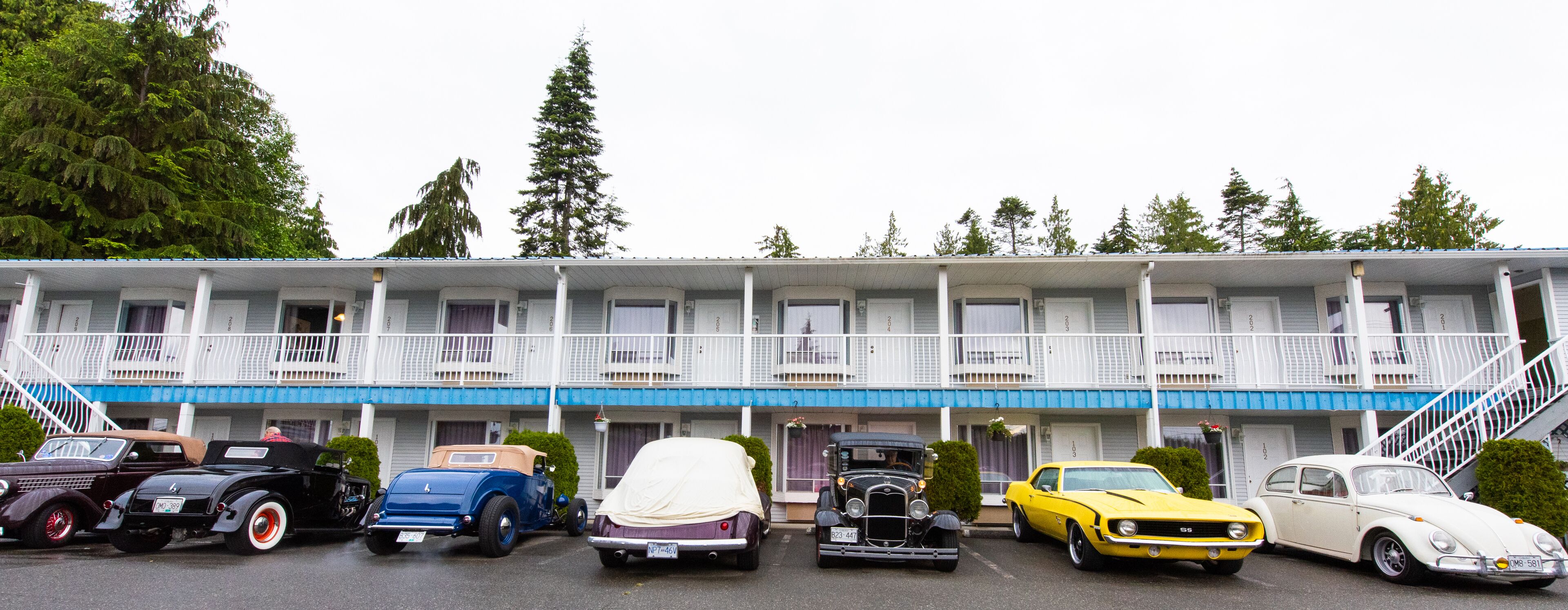 A row of vintage cars parked in front of a motel with a balcony and a staircase.