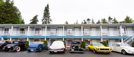 A row of vintage cars parked in front of a motel with a balcony and a staircase.