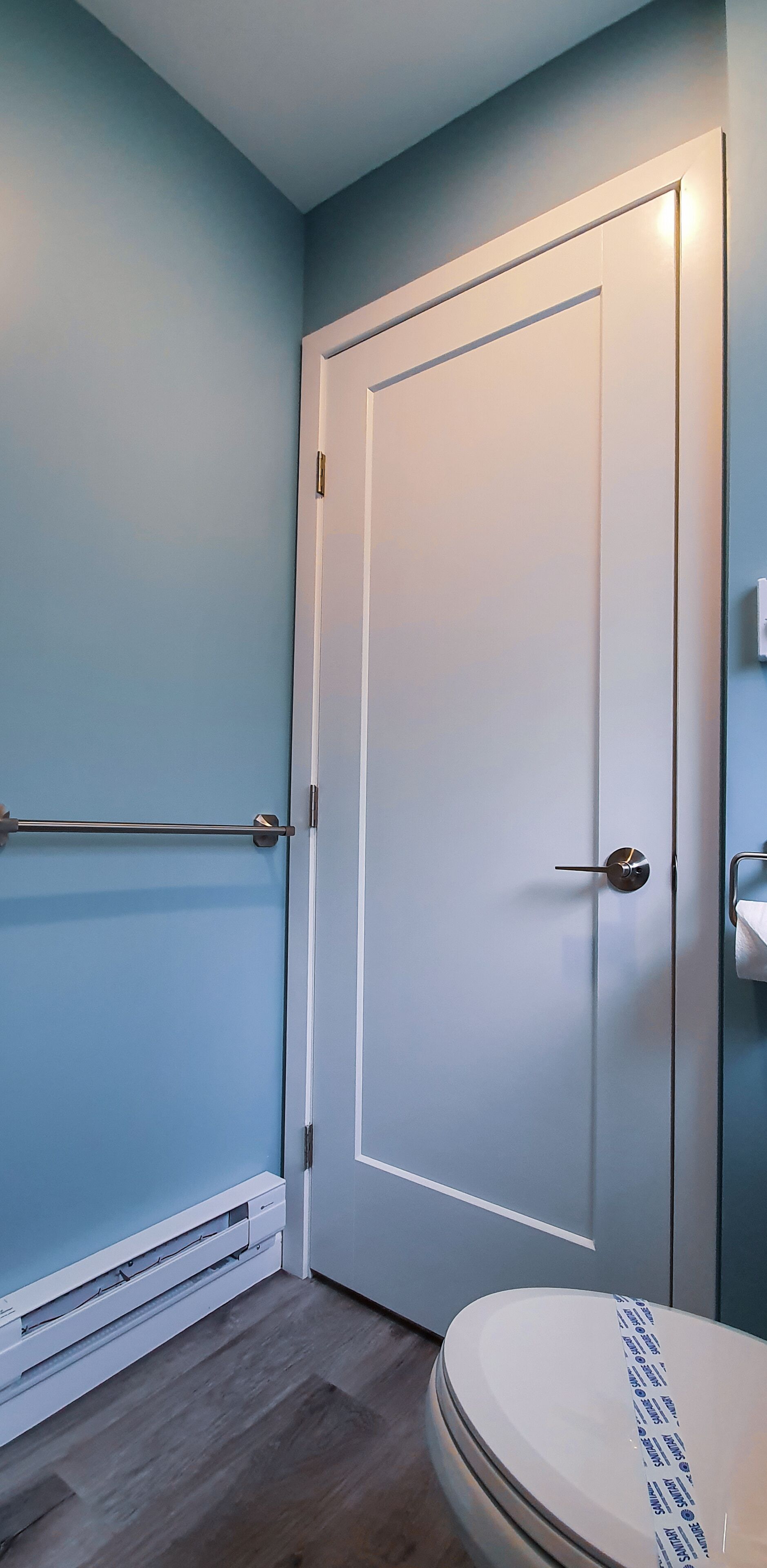 Un baño con una puerta blanca, toallero y retrete.