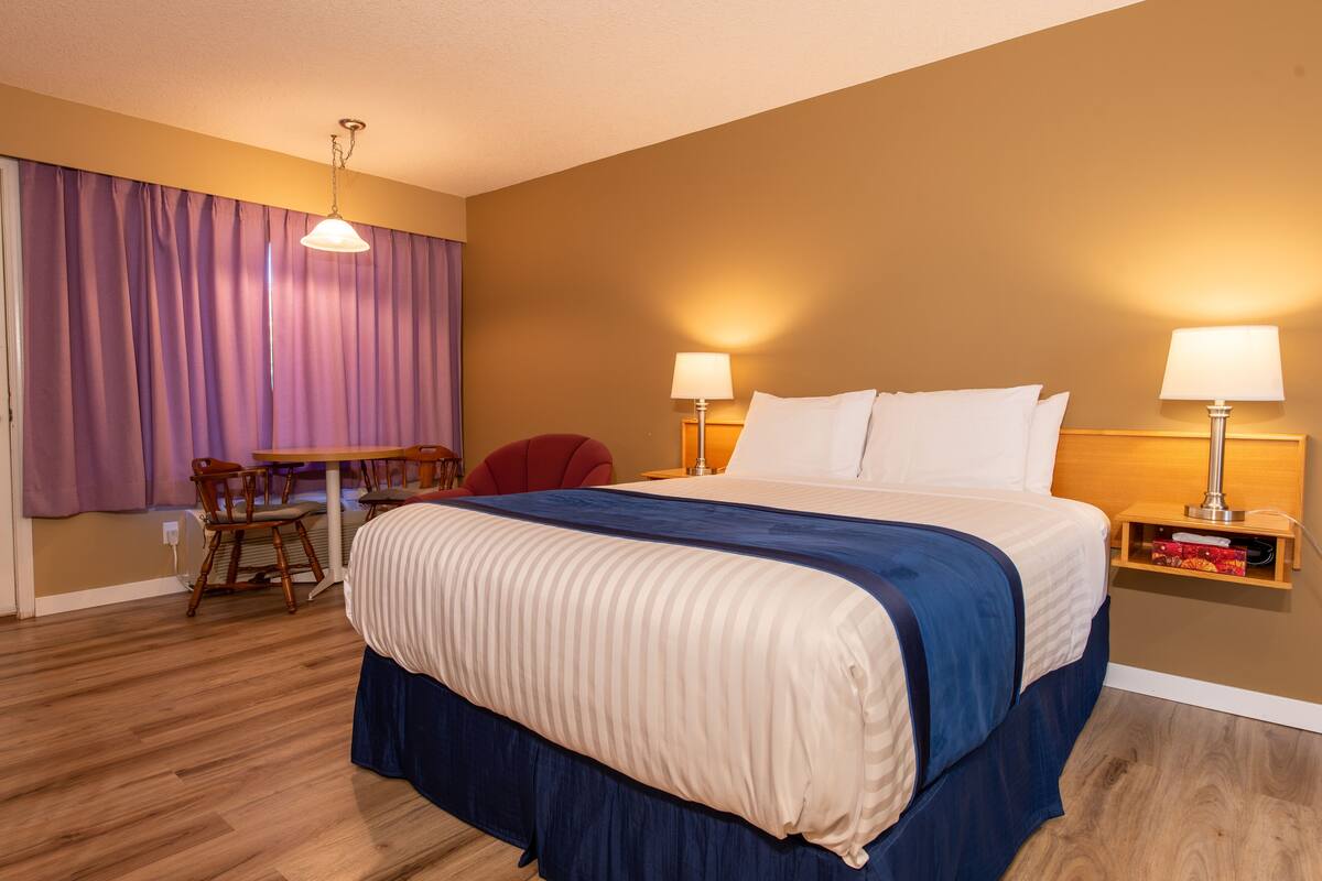 A hotel room with a bed, a desk, chairs, and two lamps.