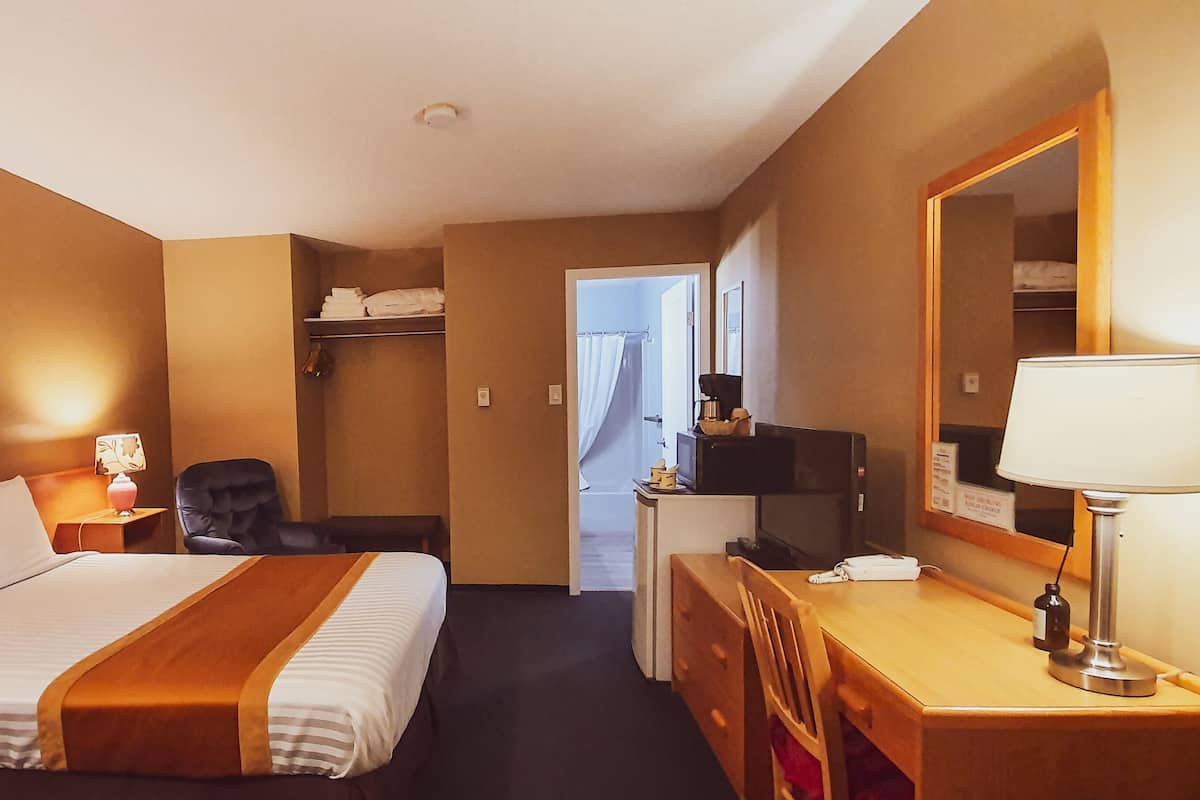 A hotel room with a bed, bedside table, lamp, chair, desk, and a mirror.