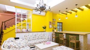 A bright yellow room with a floral sofa, a small table, and a kitchen area with a bar. - Belle Garden Yillan Villa (Dongshan)