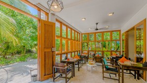 A spacious indoor dining area with large windows, wooden furniture, and a view of lush greenery outside. - Boutique Beach (Dhigurah)