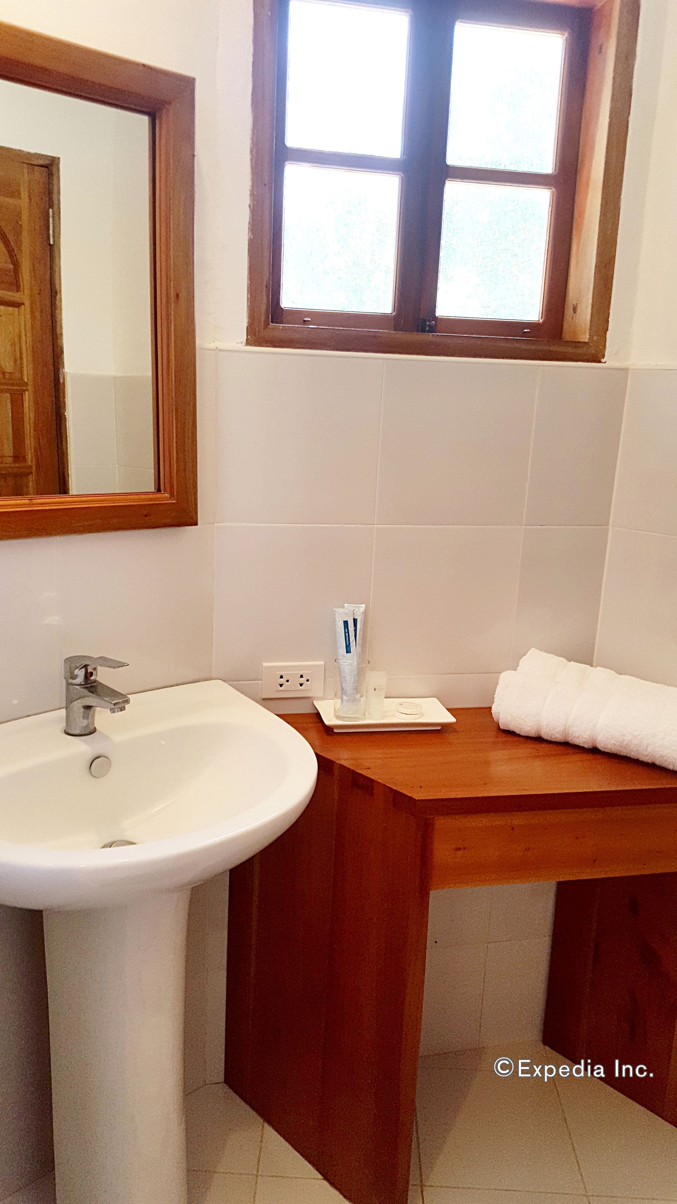 A bathroom with a white sink, wooden vanity, and a window above the mirror.